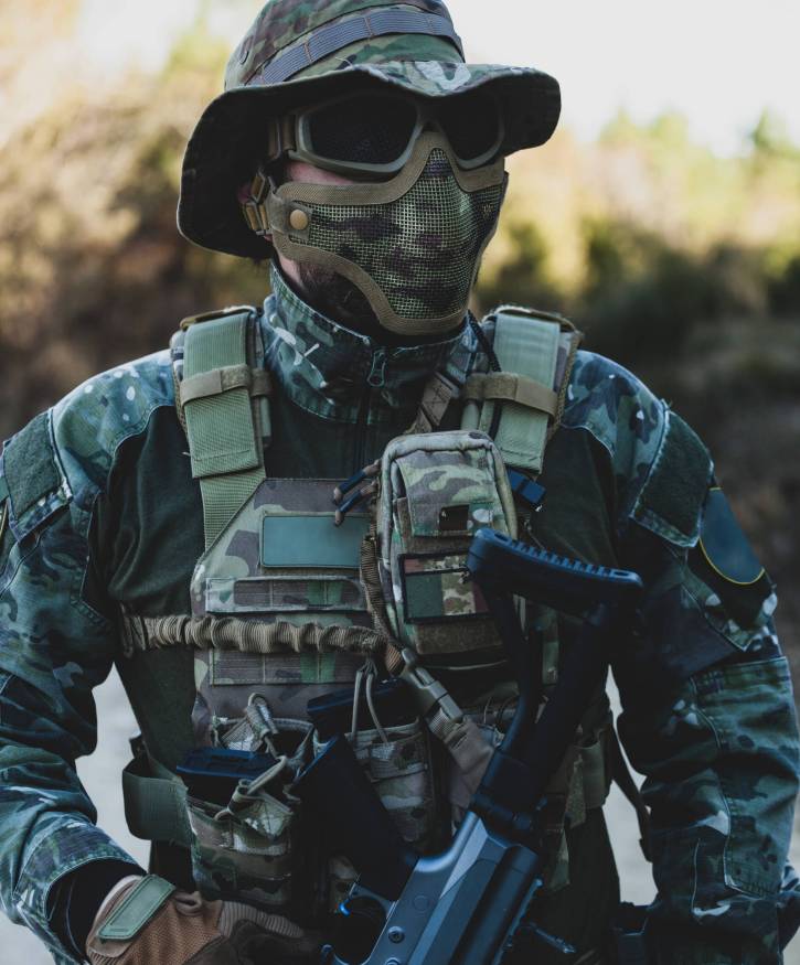 Airsoft military game player in camouflage uniform with armed assault rifle.