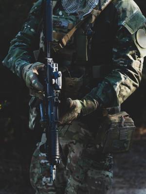 Airsoft military game player in camouflage uniform with armed assault rifle.